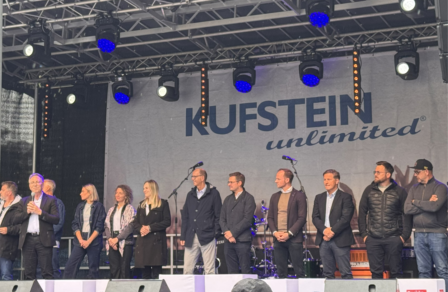 Mehrere Personen stehen bei der offiziellen Eröffnung von Kufstein Unlimited auf einer Bühne vor einem großen Banner mit der Aufschrift „Kufstein unlimited“. Fotocredit: Volksbank